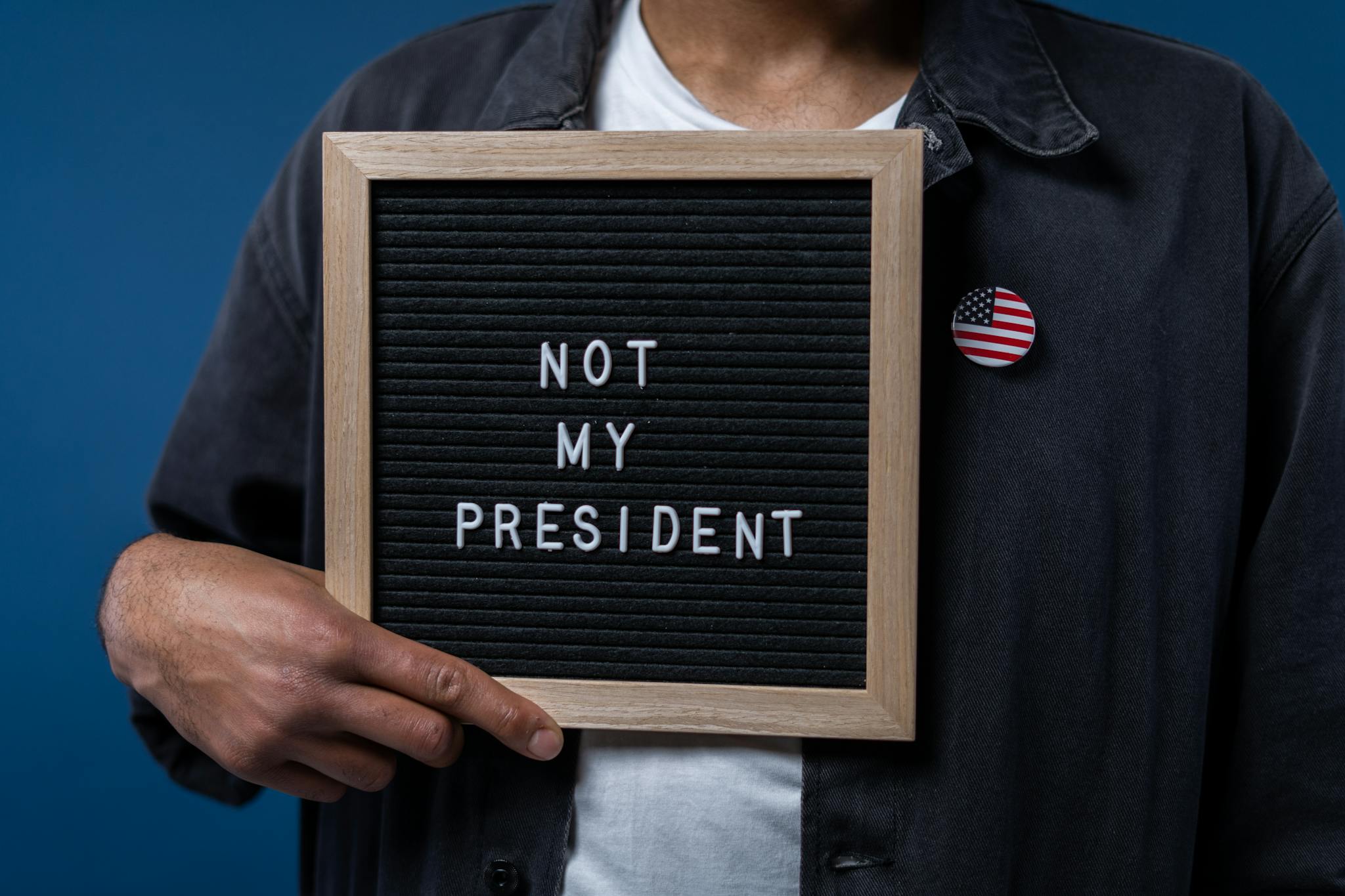 Person holding a letter board with 'Not My President' message and an American flag pin.